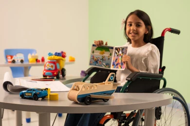 تعزيز النشاط الذهني ،  قضاء اوقات ممتعه ،  تنمية المهارات الذهنيه والفكريه في الروضات السعودية ، مفهوم هوايه المطالعه ، بنت عربيه سعوديه ترتدي الزي الكاجوال تجلس على كرسي متحرك، تقوم بعرض الكتاب التعليمي الملون بتعابير السعاده