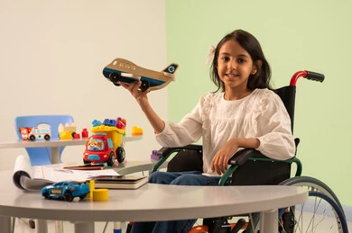 Recreational activities for people with special needs, Saudi society's interest in people with disabilities, a Saudi Arabian girl wearing casual clothes sitting in a wheelchair, playing with colorful plastic toys with happy expressions, creativity and development of mental and intellectual skills in Saudi kindergartens, encouraging, caring for and developing children's skills