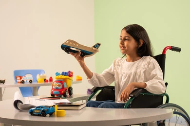 Saudi society's interest in people with disabilities, recreational activities for people with special needs, a Saudi Arabian girl wearing casual clothes sitting in a wheelchair, playing with colorful plastic toys with happy expressions, creativity and development of mental and intellectual skills in Saudi kindergartens, encouraging, caring for and developing children's skills