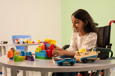 نشاطات ترفيهية لذوي الاحتياجات الخاصة ، اهتمام المجتمع السعودي بأصحاب الهمم,  قضاء اوقات ممتعه ، الابداع وتنمية المهارات الذهنيه والفكريه في الروضات السعودية ، تشجيع ورعاية وتطوير مهارات الأطفال، بنت عربيه سعوديه ترتدي الزي الكاجوال تجلس على كرسي متحرك، تقوم بتركيب المكعبات بتعابير السعاده