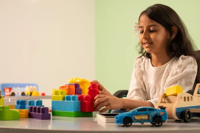 Saudi society's interest in people of determination, recreational activities for people with special needs, spending enjoyable times, creativity and developing mental and intellectual skills in Saudi kindergartens, encouraging, caring for and developing children's skills, a Saudi Arabian girl wearing casual clothes sitting in a wheelchair, assembling blocks with happy expressions