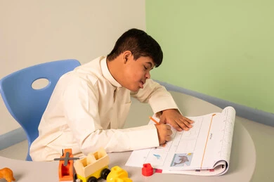 Developing mental and intellectual skills in Saudi kindergartens, expressions of focus and enjoyment, the concept of interest in hobbies, having fun, a Saudi boy with Down syndrome playing with blocks.