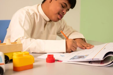 تعابير التركيز والاستمتاع ،مفهوم الاهتمام بالهوايات،  قضاء اوقات ممتعه ،تنمية المهارات الذهنيه والفكريه في الروضات السعودية ،ولد سعودي مصاب بمتلازمه داون يقوم باللعب بالمكعبات