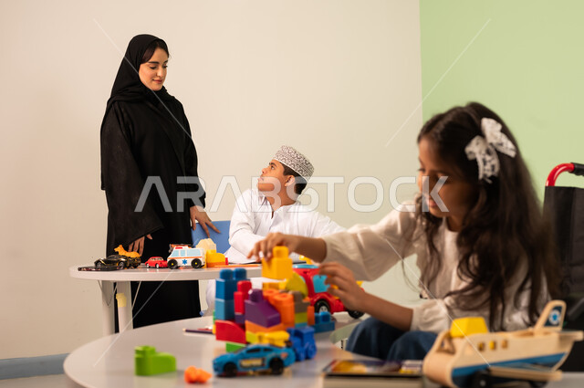 ولد سعودي مصاب بمتلازمه داون يقوم بالرسم والتلوين بالألوان برفقه معلمته، تعابير السعاده والسرور، قضاء اوقات ممتعه ،تنمية المهارات الذهنيه والفكريه في الروضات السعودية ، بنت عربية خليجية سعودية ترتدي الزي الكاجوال تجلس على كرسي متحرك وتقوم باللعب بالمكعبات ،مفهوم الاهتمام بالهوايات