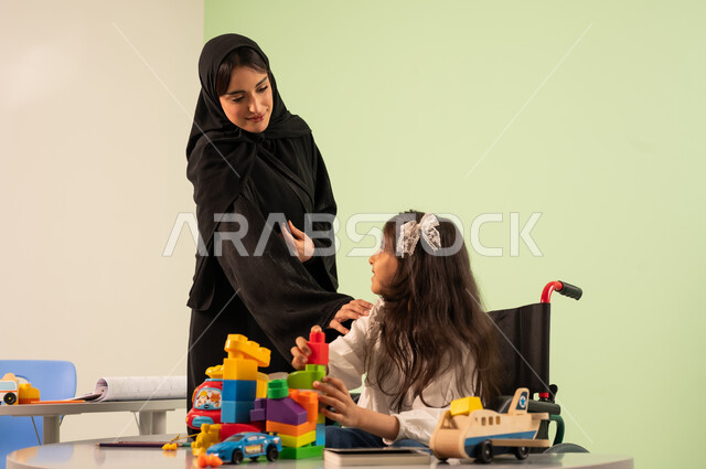 تعابير السعاده والسرور، قضاء اوقات ممتعه ،تنمية المهارات الذهنيه والفكريه في الروضات السعودية ، بنت عربية خليجية سعودية ترتدي الزي الكاجوال تجلس على كرسي متحرك وتقوم باللعب بالمكعبات ،مفهوم الاهتمام بالهوايات