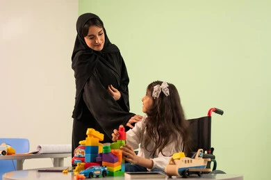 Expressions of happiness and pleasure, having a good time, developing mental and intellectual skills in Saudi kindergartens, a Saudi Arabian Gulf girl wearing casual clothes sitting in a wheelchair and playing with blocks, the concept of interest in hobbies