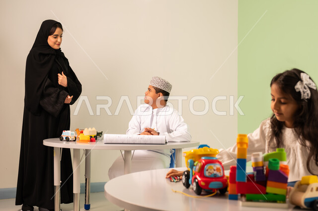 قضاء اوقات ممتعه ،تنمية المهارات الذهنيه والفكريه في الروضات السعودية ،إيماءات التركيز والاستمتاع بالرسم و التلوين،  بنت عربية خليجية سعودية ترتدي الزي الكاجوال تجلس على كرسي متحرك وتقوم باللعب بالمكعبات ،مفهوم الاهتمام بالهوايات، ولد سعودي مصاب بمتلازمه داون يقوم بالرسم والتلوين بالألوان برفقه معلمته