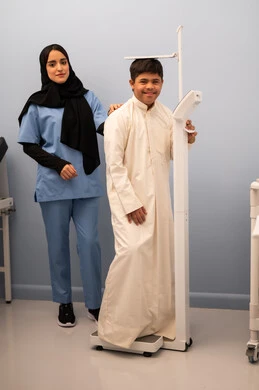 تراكم السعرات الحرارية ، مفهوم الاهتمام بالصحه واللياقه،الوزن الزائد والسمنة ، ولد عربي سعودي خليجي مصاب بمتلازمه داون ممتلئ الجسم يعاني من السمنة ، ممرضه عمانيه تستخدم ميزان لقياس الوزن ،المعاناه من مشاكل صحية