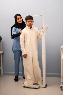 الوزن الزائد والسمنة ، تراكم السعرات الحرارية ، مفهوم الاهتمام بالصحه واللياقه، ولد عربي سعودي خليجي مصاب بمتلازمه داون ممتلئ الجسم يعاني من السمنة ، ممرضه عمانيه تستخدم ميزان لقياس الوزن ،المعاناه من مشاكل صحية