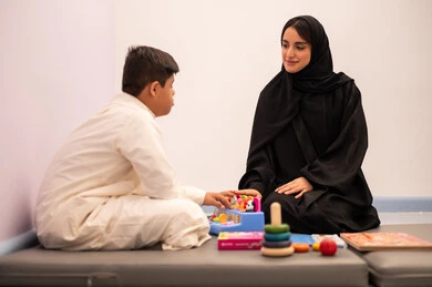 تنمية المهارات الذهنيه والفكريه في الروضات السعودية ،  مفهوم التعلم عن طريق اللعب،وسائل ايضاح ترفيفهيه للتعليم ،ايماءات التركيز والاندماج  ،ولد عربي سعودي مصاب بمتلازمه داون يقوم باللعب بلعبه الكروت التعليميه برفقه معلمته ، قضاء اوقات ممتعه