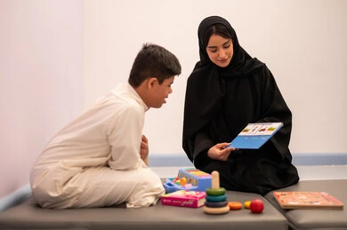 ولد عربي سعودي مصاب بمتلازمه داون يقوم باللعب بلعبه الكروت التعليميه برفقه معلمته ، مفهوم التعلم عن طريق اللعب، قضاء اوقات ممتعه  ، تنمية المهارات الذهنيه والفكريه في الروضات السعودية ،وسائل ايضاح ترفيفهيه للتعليم ،تعابير السرور والسعاده ، ايماءات التركيز والاندماج ، تعزيز النشاط الذهني