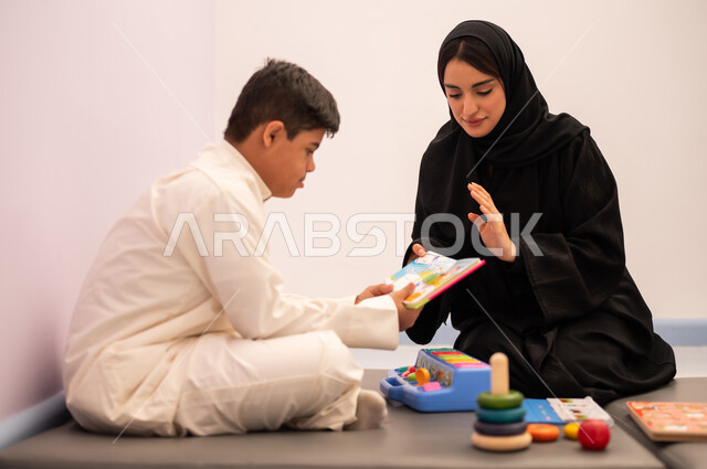 مفهوم التعلم عن طريق اللعب، قضاء اوقات ممتعه  ، تنمية المهارات الذهنيه والفكريه في الروضات السعودية ،وسائل ايضاح ترفيفهيه للتعليم ،تعابير السرور والسعاده ، ايماءات التركيز والاندماج ، تعزيز النشاط الذهني، ولد عربي سعودي مصاب بمتلازمه داون يقوم باللعب بلعبه الكروت التعليميه برفقه معلمته