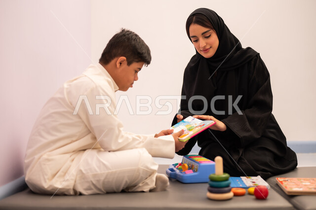 قضاء اوقات ممتعه  ، تنمية المهارات الذهنيه والفكريه في الروضات السعودية ،وسائل ايضاح ترفيفهيه للتعليم ،تعابير السرور والسعاده ، ايماءات التركيز والاندماج ، تعزيز النشاط الذهني، مفهوم هوايه المطالعه ، ولد عربي سعودي مصاب بمتلازمه داون يقوم باللعب بلعبه الكروت التعليميه برفقه معلمته