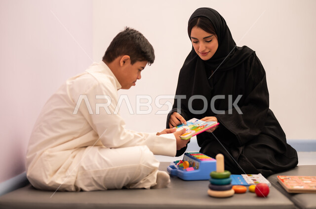 تنمية المهارات الذهنيه والفكريه في الروضات السعودية ،قضاء اوقات ممتعه  ،وسائل ايضاح ترفيفهيه للتعليم ،تعابير السرور والسعاده ، ايماءات التركيز والاندماج ، تعزيز النشاط الذهني، مفهوم هوايه المطالعه ، ولد عربي سعودي مصاب بمتلازمه داون يقوم باللعب بلعبه الكروت التعليميه برفقه معلمته