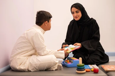 ايماءات التركيز والاندماج ،   تعزيز النشاط الذهني، مفهوم هوايه المطالعه ، ولد عربي سعودي مصاب بمتلازمه داون يقوم باللعب بلعبه الكروت التعليميه برفقه معلمته، تنمية المهارات الذهنيه والفكريه في الروضات السعودية ،وسائل ايضاح ترفيفهيه للتعليم ،تعابير السرور والسعاده ، قضاء اوقات ممتعه