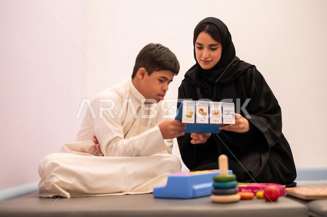 التعلم عن طريق اللعب، ولد عربي سعودي مصاب بمتلازمه داون يقوم باللعب بلعبه الكروت التعليميه برفقه معلمته، تنمية المهارات الذهنيه والفكريه في الروضات السعودية ،وسائل ايضاح ترفيفهيه للتعليم ، تعزيز النشاط الذهني، ايماءات التركيز والاندماج ،تعابير السرور والسعاده ، قضاء اوقات ممتعه