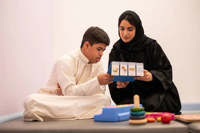 Learning through play, a Saudi Arabian boy with Down syndrome playing educational cards with his teacher, developing mental and intellectual skills in Saudi kindergartens, educational entertainment means, enhancing mental activity, gestures of concentration and integration, expressions of pleasure and happiness, spending enjoyable times