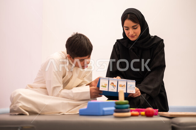 ولد عربي سعودي مصاب بمتلازمه داون يقوم باللعب بلعبه الكروت التعليميه برفقه معلمته، تنمية المهارات الذهنيه والفكريه في الروضات السعودية ،وسائل ايضاح ترفيفهيه للتعليم ، تعزيز النشاط الذهني، ايماءات التركيز والاندماج ،تعابير السرور والسعاده ، قضاء اوقات ممتعه