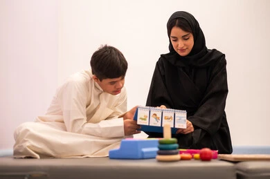 ولد عربي سعودي مصاب بمتلازمه داون يقوم باللعب بلعبه الكروت التعليميه برفقه معلمته، تنمية المهارات الذهنيه والفكريه في الروضات السعودية ،وسائل ايضاح ترفيفهيه للتعليم ، تعزيز النشاط الذهني، ايماءات التركيز والاندماج ،تعابير السرور والسعاده ، قضاء اوقات ممتعه