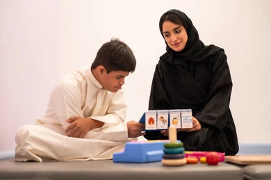 تنمية المهارات الذهنيه والفكريه في الروضات السعودية ،وسائل ايضاح ترفيفهيه للتعليم ، تعزيز النشاط الذهني، ايماءات التركيز والاندماج ،تعابير السرور والسعاده ، قضاء اوقات ممتعه ،  ولد عربي سعودي مصاب بمتلازمه داون يقوم باللعب بلعبه الكروت التعليميه برفقه معلمته