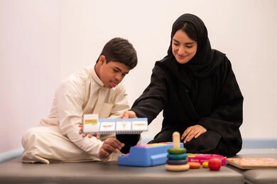 Educational entertainment aids, enhancing mental activity, gestures of concentration and integration, expressions of pleasure and happiness, developing mental and intellectual skills in Saudi kindergartens, having fun, a Saudi Arabian boy with Down syndrome playing an educational card game with his teacher