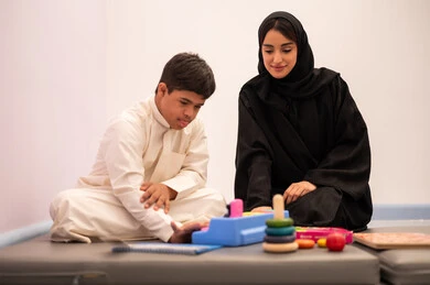 Developing mental and intellectual skills in Saudi kindergartens, having fun, enhancing mental activity, gestures of concentration and integration, expressions of pleasure and happiness, a Saudi Arabian boy with Down syndrome playing an educational card game with his teacher.