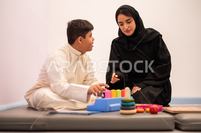 قضاء اوقات ممتعه ،تعزيز النشاط الذهني، ايماءات التركيز والاندماج ،تعابير السرور والسعاده ، تنمية المهارات الذهنيه والفكريه في الروضات السعودية ،  ولد عربي سعودي مصاب بمتلازمه داون يقوم باللعب بلعبه الكروت التعليميه برفقه معلمته