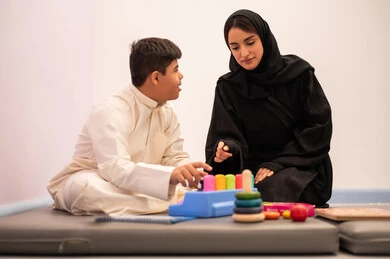 قضاء اوقات ممتعه ،تعزيز النشاط الذهني، ايماءات التركيز والاندماج ،تعابير السرور والسعاده ، تنمية المهارات الذهنيه والفكريه في الروضات السعودية ،  ولد عربي سعودي مصاب بمتلازمه داون يقوم باللعب بلعبه الكروت التعليميه برفقه معلمته