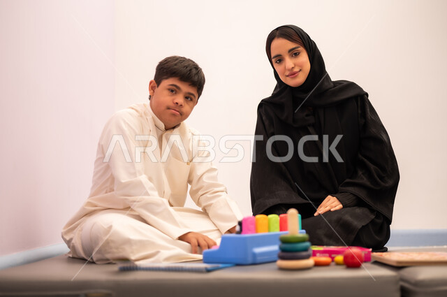 Expressions of pleasure and happiness, developing mental and intellectual skills in Saudi kindergartens, having fun, enhancing mental activity, gestures of concentration and integration, a Saudi Arabian boy with Down syndrome playing an educational card game with his teacher