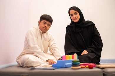 Expressions of pleasure and happiness, developing mental and intellectual skills in Saudi kindergartens, having fun, enhancing mental activity, gestures of concentration and integration, a Saudi Arabian boy with Down syndrome playing an educational card game with his teacher