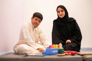Developing mental and intellectual skills in Saudi kindergartens, expressions of pleasure and happiness, having fun, enhancing mental activity, gestures of concentration and integration, a Saudi Arabian boy with Down syndrome playing an educational card game with his teacher.