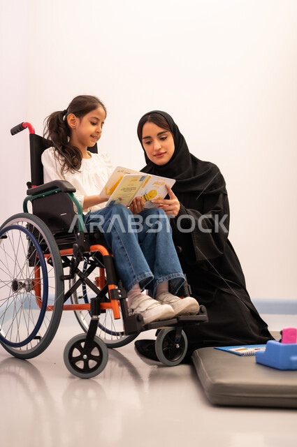مفهوم هوايه المطالعه ،تعزيز النشاط الذهني، قضاء اوقات ممتعه ،تنمية المهارات الذهنيه والفكريه في الروضات السعودية ، بنت عربيه سعوديه ترتدي الزي الكاجوال تجلس على كرسي متحرك، تقوم بقراءه الكتب التعليميه الملونه برفقه معلمتها ، تعابير السرور والسعاده