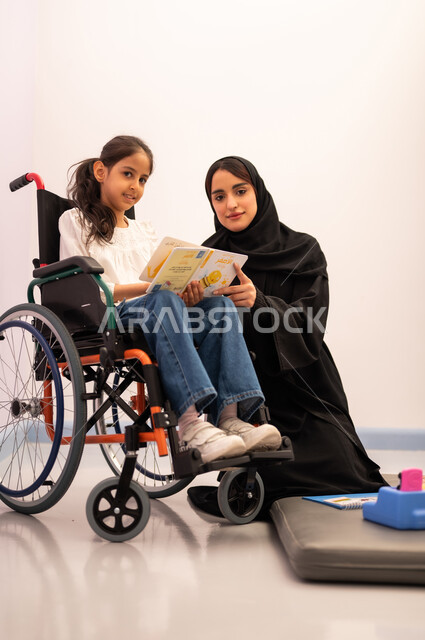 تعزيز النشاط الذهني، قضاء اوقات ممتعه ،تنمية المهارات الذهنيه والفكريه في الروضات السعودية ،  مفهوم هوايه المطالعه ،بنت عربيه سعوديه ترتدي الزي الكاجوال تجلس على كرسي متحرك، تقوم بقراءه الكتب التعليميه الملونه برفقه معلمتها ، تعابير السرور والسعاده