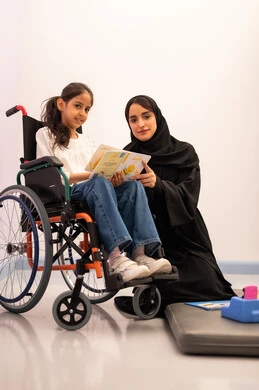 تعزيز النشاط الذهني، قضاء اوقات ممتعه ،تنمية المهارات الذهنيه والفكريه في الروضات السعودية ،  مفهوم هوايه المطالعه ،بنت عربيه سعوديه ترتدي الزي الكاجوال تجلس على كرسي متحرك، تقوم بقراءه الكتب التعليميه الملونه برفقه معلمتها ، تعابير السرور والسعاده