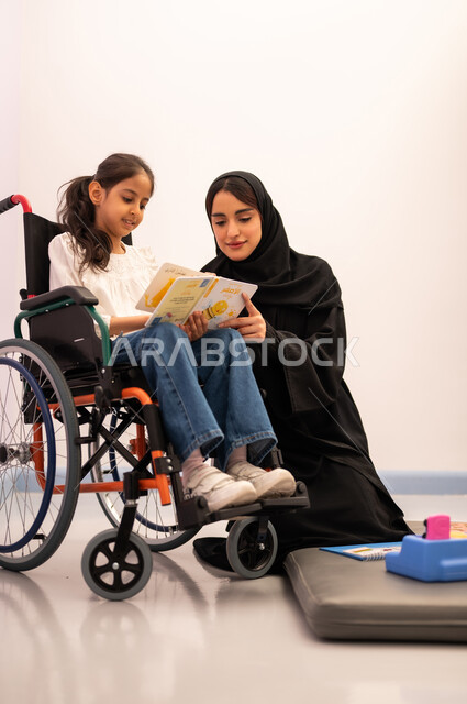 قضاء اوقات ممتعه ،تنمية المهارات الذهنيه والفكريه في الروضات السعودية ،  تعزيز النشاط الذهني،  مفهوم هوايه المطالعه ،بنت عربيه سعوديه ترتدي الزي الكاجوال تجلس على كرسي متحرك، تقوم بقراءه الكتب التعليميه الملونه برفقه معلمتها ، تعابير السرور والسعاده