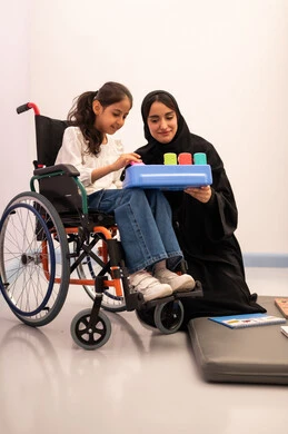 ايماءات التركيز والاندماج ، تنمية المهارات الذهنيه والفكريه في الروضات السعودية ، تعزيز النشاط الذهني، قضاء اوقات ممتعه ،بنت عربيه سعوديه ترتدي الزي الكاجوال تجلس على كرسي متحرك، تقوم باللعب بلعبه الكروت المطابقه برفقه معلمتها ، تعابير السرور والسعاده