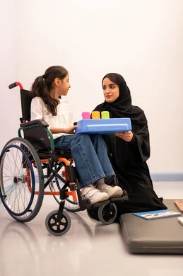 تنمية المهارات الذهنيه والفكريه في الروضات السعودية ، تعزيز النشاط الذهني، قضاء اوقات ممتعه ،بنت عربيه سعوديه ترتدي الزي الكاجوال تجلس على كرسي متحرك، تقوم باللعب بلعبه الكروت المطابقه برفقه معلمتها ، تعابير السرور والسعاده