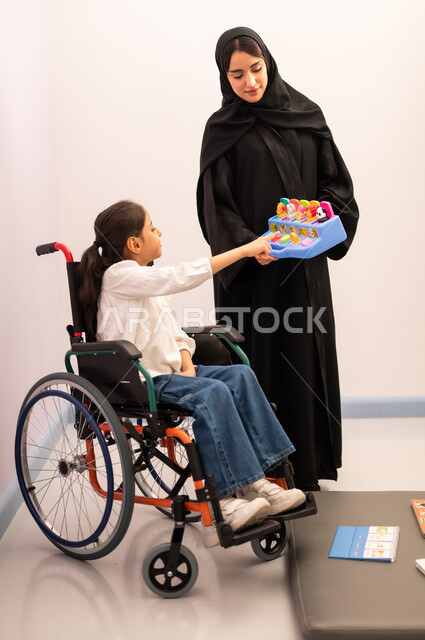 قضاء اوقات ممتعه ،تنمية المهارات الذهنيه والفكريه في الروضات السعودية ، تعزيز النشاط الذهني، بنت عربيه سعوديه ترتدي الزي الكاجوال تجلس على كرسي متحرك، تقوم باللعب بلعبه الكروت المطابقه برفقه معلمتها ، تعابير السرور والسعاده
