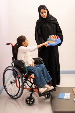 قضاء اوقات ممتعه ،تنمية المهارات الذهنيه والفكريه في الروضات السعودية ، تعزيز النشاط الذهني، بنت عربيه سعوديه ترتدي الزي الكاجوال تجلس على كرسي متحرك، تقوم باللعب بلعبه الكروت المطابقه برفقه معلمتها ، تعابير السرور والسعاده