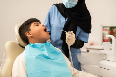 تقديم الخدمات الطبية للمرضى, العناية بالصحة الفموية،استخدام الأدوات المعقمة لإجراء الفحوصات السنية،ولد سعودي مصاب بمتلازمة داون  يجلس على كرسي العلاج ، طبيبة ترتدي القفازات والكمامه تقوم بفحص أسنان المريض، مفهوم الطب والرعاية الصحية