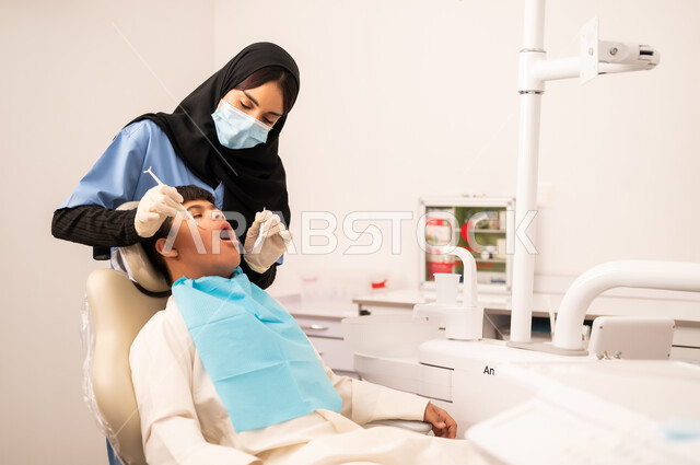 استخدام الأدوات المعقمة لإجراء الفحوصات السنية،العناية بالصحة الفموية ، مفهوم الطب والرعاية الصحية، طبيبة ترتدي القفازات والكمامه تقوم بفحص أسنان المريض، تقديم الخدمات الطبية للمرضى,ولد سعودي مصاب بمتلازمة داون  يجلس على كرسي العلاج