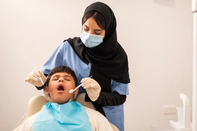 ولد سعودي مصاب بمتلازمة داون  يجلس على كرسي العلاج ، استخدام الأدوات المعقمة لإجراء الفحوصات السنية،العناية بالصحة الفموية، طبيبة ترتدي القفازات والكمامه تقوم بفحص أسنان المريض، تقديم الخدمات الطبية للمرضى,مفهوم الطب والرعاية الصحية