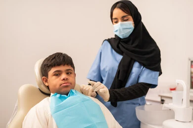 Oral health care. A doctor wearing gloves and a mask examines a patient's teeth. The concept of medicine and healthcare. Using sterile tools for dental examinations. Providing medical services to patients. A Saudi boy with Down syndrome sitting in a treatment chair.