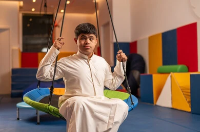 Gestures of focus and seriousness, having a wonderful time at an amusement park, a Saudi boy with Down syndrome at an amusement park, playing on the fun swings, enjoying summer vacation, fun and entertainment.