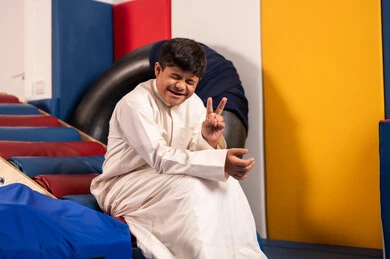 Enjoying summer vacation, gestures of joy and happiness, having a wonderful time at an amusement park, times of entertainment and leisure, a Saudi boy with Down syndrome at an amusement park, playing a fun slide game, raising his hand in a victory sign.