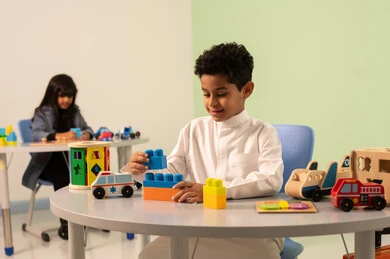 Performing many fun activities, a Gulf Arab Omani girl in casual attire engages in skills and activities, developing mental and intellectual skills, taking care of children's skills, kindergartens and nurseries, a Saudi boy playing with colored blocks.