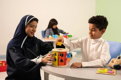 أداء الكثير من الأنشطة الممتعة، معلمة عربية عمانيه لرياض أطفال تختص بالاعتناء بالاطفال، رياض الأطفال والحاضنات، ولد عربي خليجي عماني يرتدي الزي العماني التقليدي يقوم بالمهارات والانشطه برفقه معلمته ، بنت عمانية تلعب بالالعاب البلاستيكيه