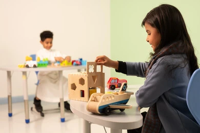 Caring for children's skills, kindergartens and nurseries, performing many fun activities, an Arab Gulf Omani girl wearing casual attire engaging in skills and activities, a Saudi boy playing with colorful plastic toys.