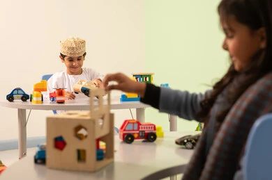 Kindergartens and nurseries, performing many fun activities, taking care of children's skills, an Arab Gulf Omani girl wearing casual attire engaging in skills and activities, a Saudi boy playing with colorful plastic toys.
