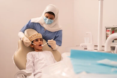 إجراء الفحوصات الدورية للعناية بالصحة الفموية، ولد عربي خليجي عماني يرتدي الزي العماني التقليدي  يجلس على كرسي العلاج في العيادة السنية،مفهوم الطب والرعاية الصحية، استخدام المعدات اللازمة لجراحة الاسنان ، طبيبة ترتدي القفازات تقوم بفحص أسنان المريض،  تقديم الخدمات الطبية للمرضى